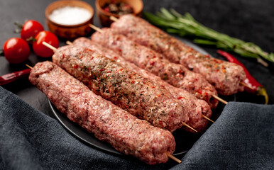 raw Lula kebab on skewers with spices in a black plate on a stone background