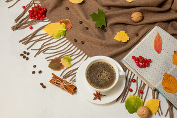 Autumn cozy composition. Coffee in a Cup, brown scarf, book, cinnamon sticks, fallen leaves on a white table. Selective focus.