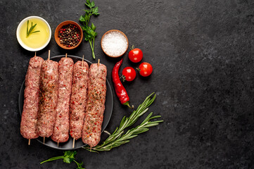 raw Lula kebab on skewers with spices in a black plate on a stone background with copy space for your text