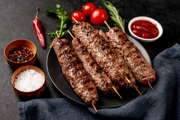 Grilled Lula kebab on skewers with spices in a black plate on a stone background