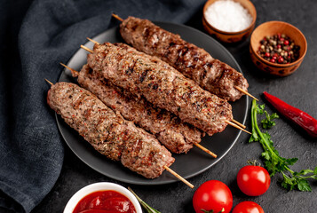 Grilled Lula kebab on skewers with spices in a black plate on a stone background