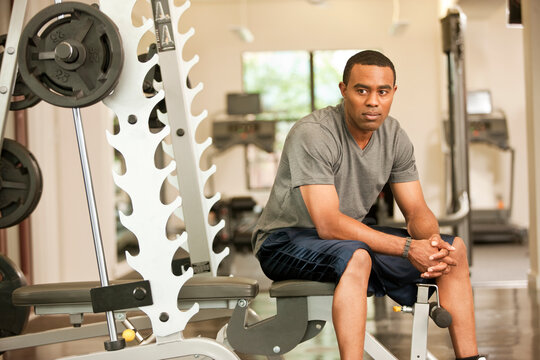 African American man resting in health club on weight-lifting bench
