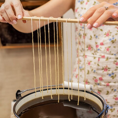 Candle Making Process of natural wax . A woman holding ropes wicks over hot wax.