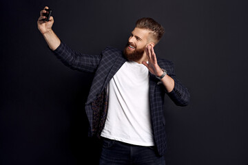 Handsome bearded businessman in suit making selfie isolated on black