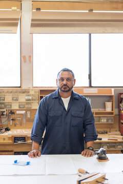 Hispanic woodshop worker looks at the camera with a serious fac