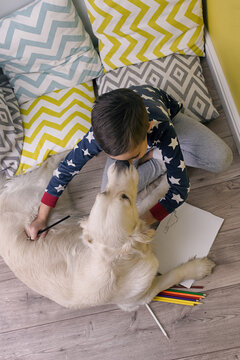 Child embracing dog while drawing