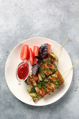 Snacks. Shish kebab on skewers. Fried zucchini slices, bacon and chicken on a white plate with red sweet lingonberry sauce. Tomatoes, herbs and basil. Flatlay. Background image, copy space
