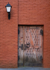 Antique wooden door with metal hinges on a red brick wall.