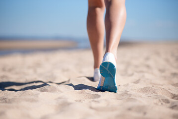 sports female legs in sneakers on the beach against the background of the blue sea. The sportswoman runs on the sand.