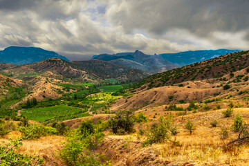 Fototapeta na wymiar Landscape of the Crimean mountains, covered by approaching storm clouds, and a valley with vineyards