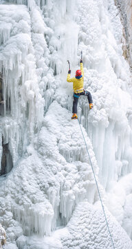 Male ice climber ascending on frozen waterfall