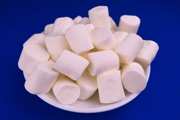 Full bowl with marshmallows on a blue background.
Close-up.