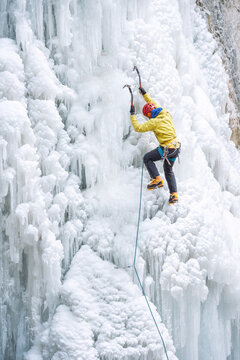 Male alpinist ascending on frozen waterfall
