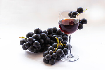 Black grapes and red wine in a glass on a white background