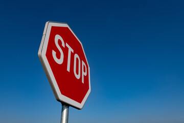 Stop Schild Verkehrsschild Halt Straße anhalten blauer Himmel rot weiß reflektierend Folie Buchstaben Straßenverkehrsordnung Deutschland international Symbol Achteck Oktagon achteckig Tafel Mast Sonne