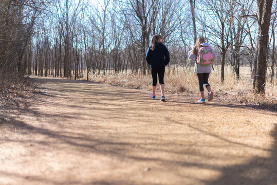 Two Young Girls Walk Along A Gravel Path Among Trees