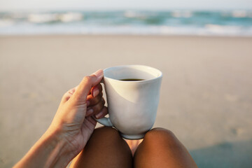 woman holding a cup of coffee in the morning on the beach
