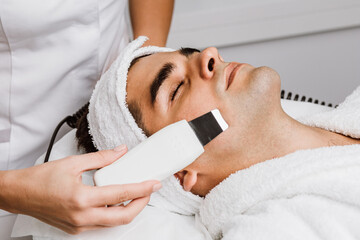 Good looking man receiving ultrasound cavitation facial peeling. Skin cleansing procedure at beauty spa salon.
