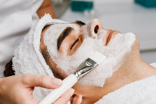 Good looking man receiving facial mask with rejuvenating effects in spa beauty salon.