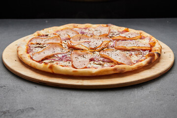 Delicious Italian Pizza with ham, onions and mozzarella cheese on dark background
