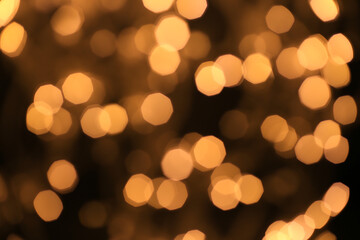 Christmas and Happy New Year on blurred bokeh of gold color on black background, glowing sparks, holiday lights, place for text