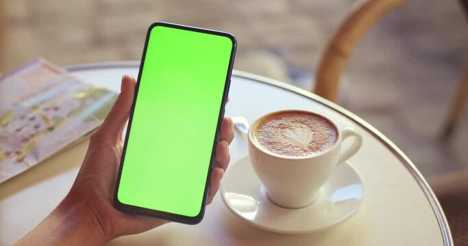Crop view of female hands with trendy fingernails design holding mobilephone with mockup screen while having cup of coffee. Concept of greenscreen and chroma key.