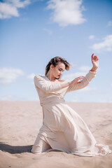 Fototapeta na wymiar A young, slender girl in a beige dress poses in the wind in the desert