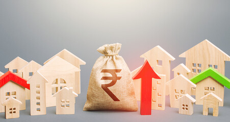 Indian rupee money bag and a city of house figures and red up arrow. Recovery and growth in...