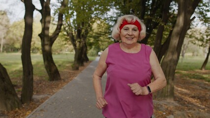 Senior old woman running in park and using smart watch. Female runner working out cardio outdoor