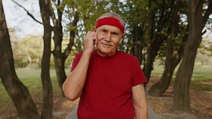 Naklejka na ściany i meble Senior old runner man in city park and using bluetooth earphones and listening music