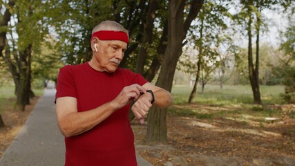 Senior runner man in park using smart watch, tracking distance, checking pulse after fitness workout