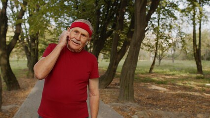Senior old runner man in city park and using bluetooth earphones and listening music