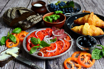 Fototapeta na wymiar Tomatoes, croissants, fruits, olives and bread on serving plates on a wooden background.