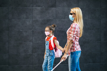Fototapeta na wymiar Young blind mother walking with her little daughter on city street. They wearing face protective masks. Back to school and new coronavirus lifestyle concept.