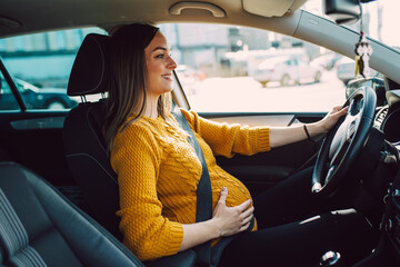 Pregnant happy woman driving with safety belt on in the car.