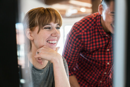 Two young business people laughing as they look at computer moni