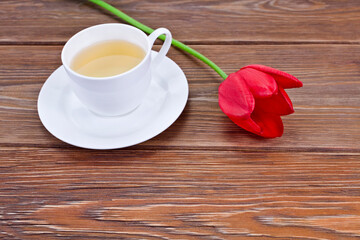 Cup of green tea with red tulip flower on a wooden background.