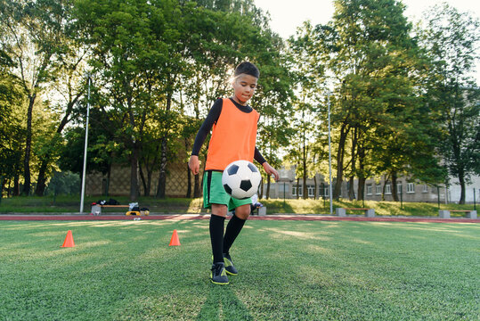 Diligent teen football player stuffs soccer ball on feet with boots. Practicing sport exercises at artificial stadium.