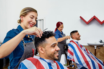 Two women hairdressers in the barbershop cutting the hair of customers.