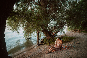 An attractive blonde caucasian woman lies in the arms of a man on the beach. A loving couple on a picnic by the river