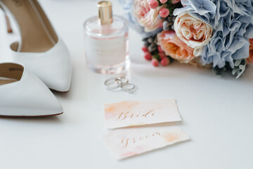 Wedding accessory bride. Stylish beige shoes, earrings, gold rings, flowers, garter, perfumes on table standing on wooden background. Letters from the bride and groom. flat lay. top view.