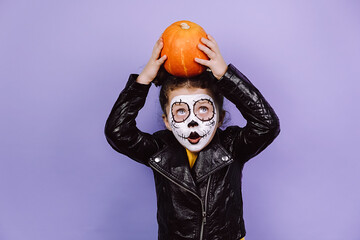 Portrait of shocked little child girl holds on his head orange pumpkin, looking at up, wears black...