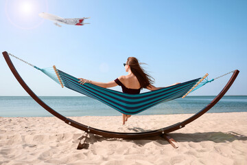 Young woman relaxing in hammock on beach under blue sky with flying plane. Summer vacation