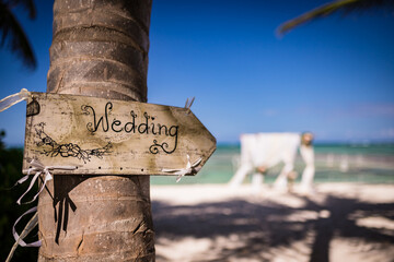 Close up view of wedding wooden plate on the palm tree and colorful decorated wedding bamboo gazebo on the paradise beach of Caribbean Sea at the background, Punta Cana, Dominican Republic  