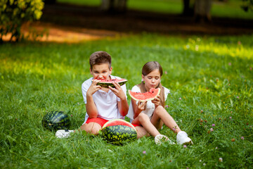boy and girl sit on the grass and eat watermelon
