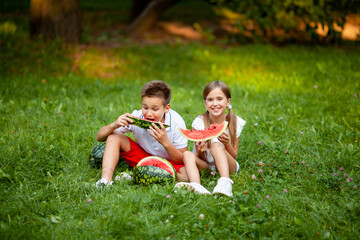 Fototapeta premium boy and girl sit on the grass and eat watermelon