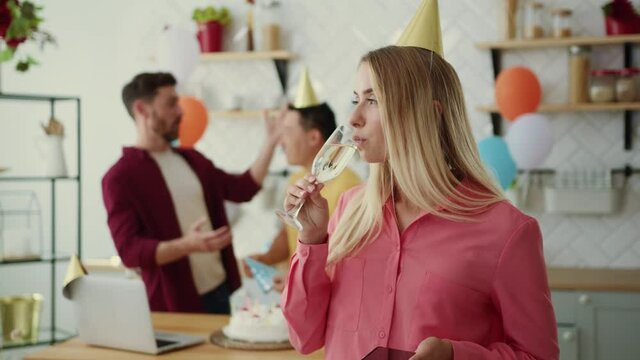 Bored sad blonde woman drinking champagne using smartphone on birthday party. Upset girl feeling lonely on holidays while her friends celebrating anniversary.