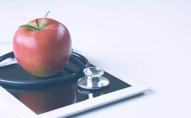Medical stethoscope and red apple lying on a tablet isolated on white background.