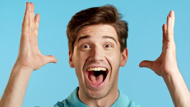 Close-up face of amazed european man shocked, saying WOW. Handsome guy surprised to camera over blue background.