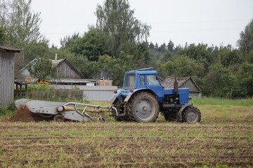 Old wheeled tractor with potato harvesting attachments in the field, rural potatoes harvesting on an autumn day on old wooden barn background, Russian countryside farm beautiful view